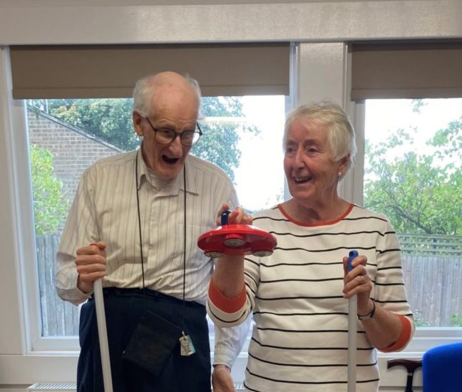 Photograph of elderly man and women stood together playing version of hockey